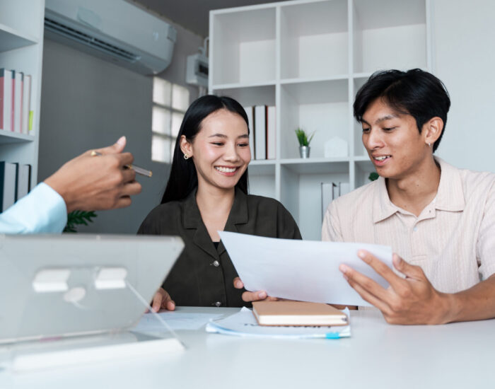A young couple consults with a financial planner, reviewing documents and discussing investment strategies in a contemporary office environment.