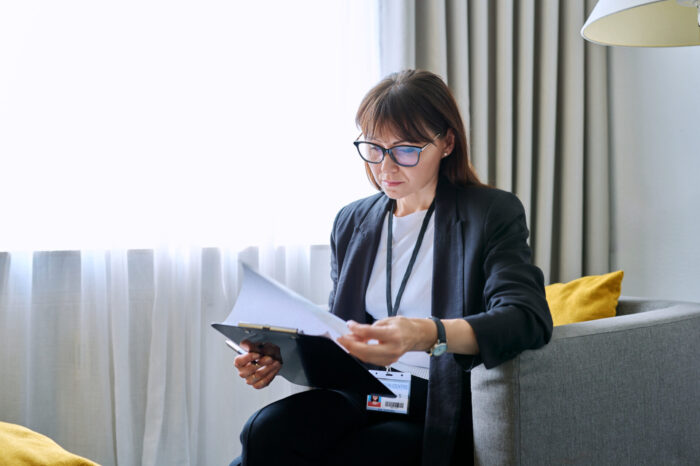 Portrait of middle-aged woman with clipboard sitting in an office chair. Mature friendly female professional mental specialist, psychologist, psychotherapist, therapist, social worker, workplace counselor